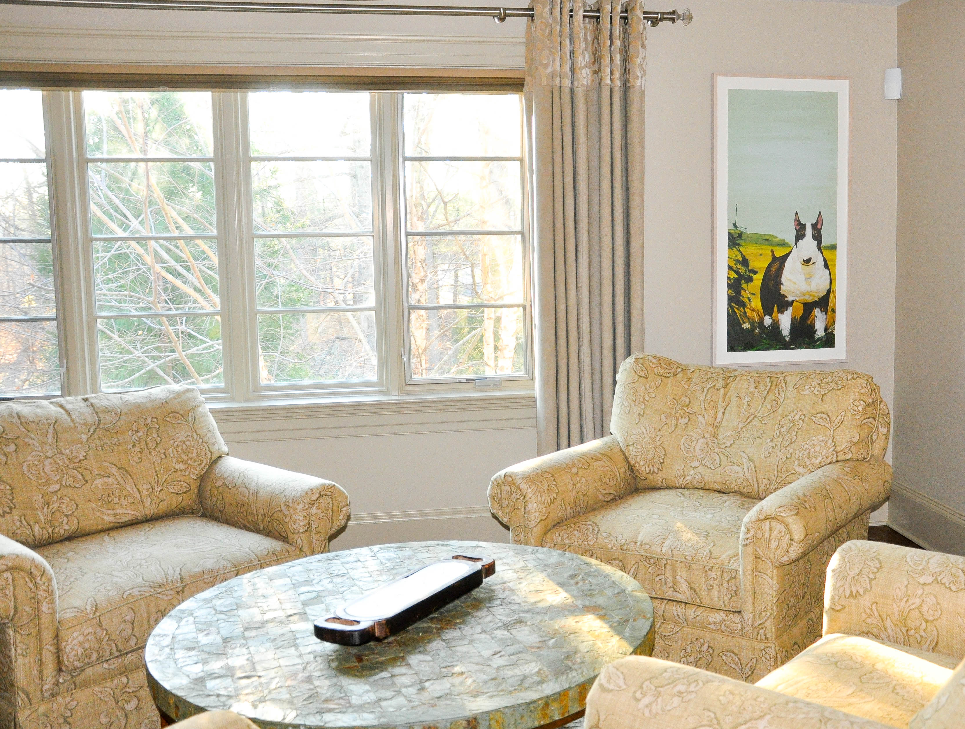 A gorgeous light-filled lounge area showcases a row of large windows and a framed art print of a black and white terrier dog.